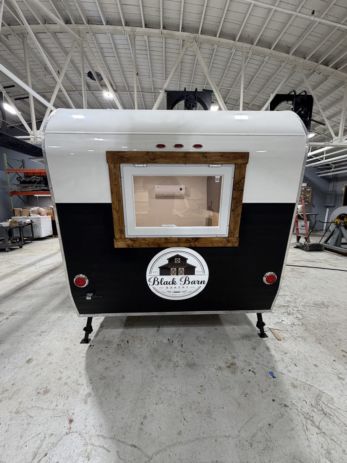 Rear of the Black Barn Bakery trailer in the shop, with barn logos and a wood-framed window