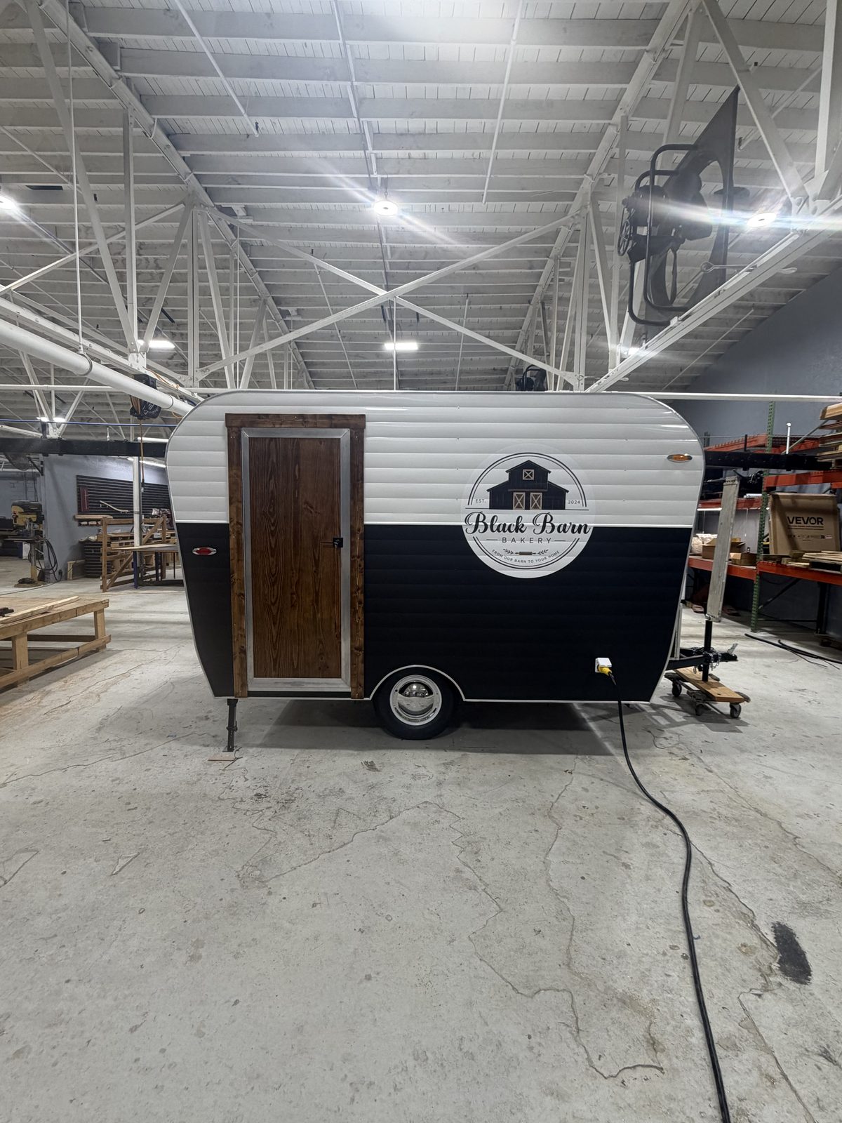 Door side of the Black Barn Bakery trailer with a wood entry door and bakery logo
