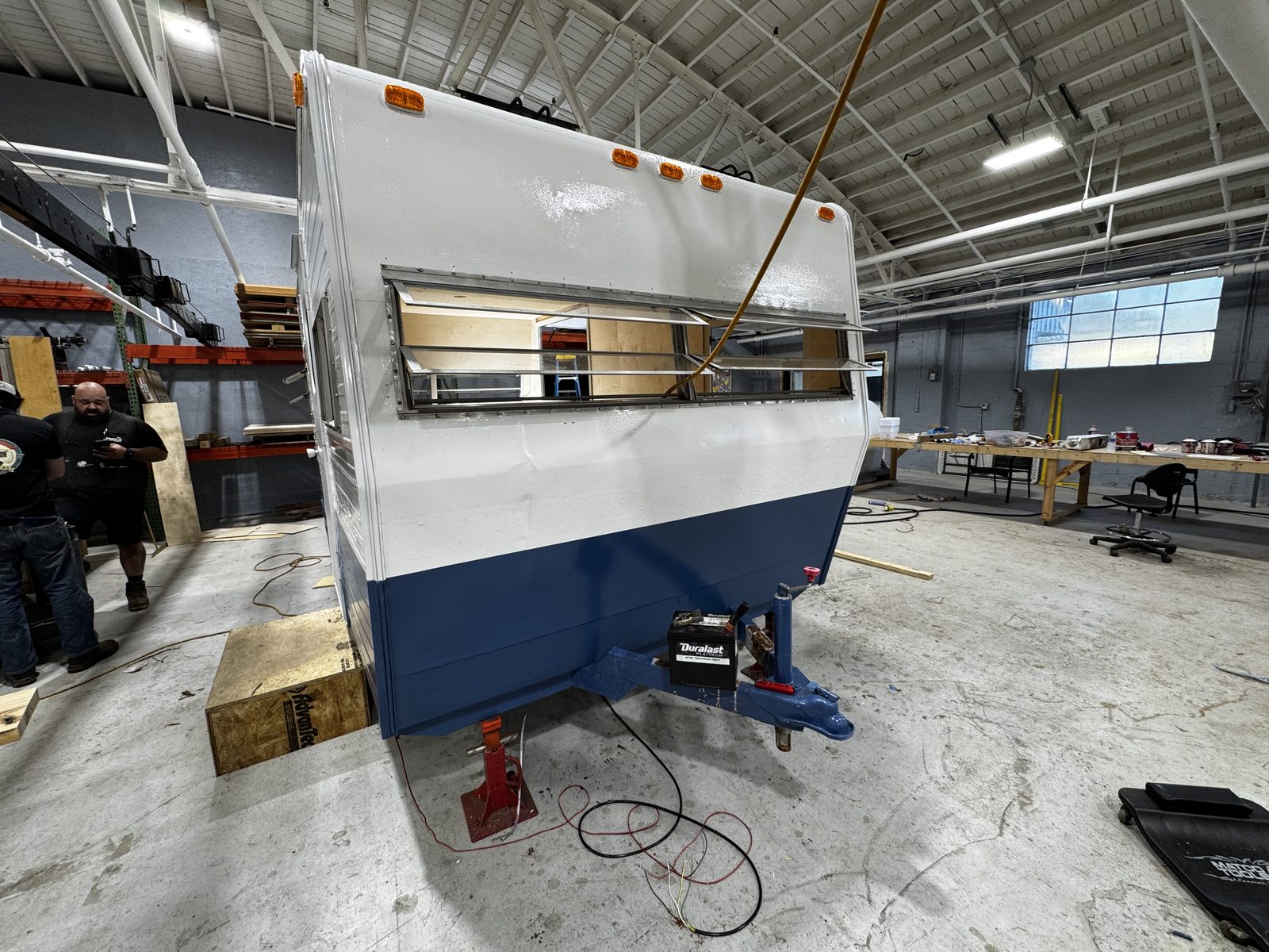 Front quarter of the white-over-navy trailer on a jack, service hatch open